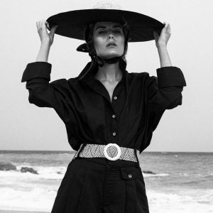Camisa Miyako negra hecha de lino y algodon organico con mangas corte japones, puño vuelto y cuello con cuerpo para mantenerse alto, modelo con outfit negro y sombrero en la playa